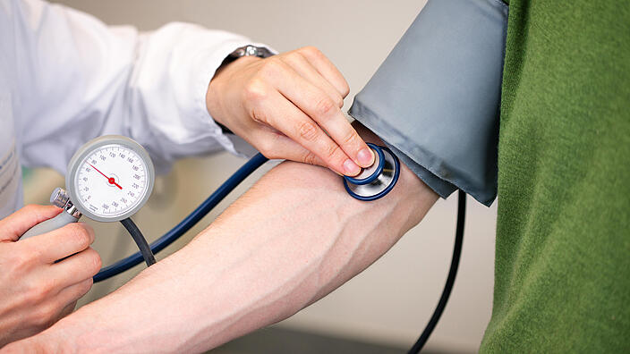  Arzt überprüft mit Blutdruckmessgerät den Blutdruck eines Patienten.