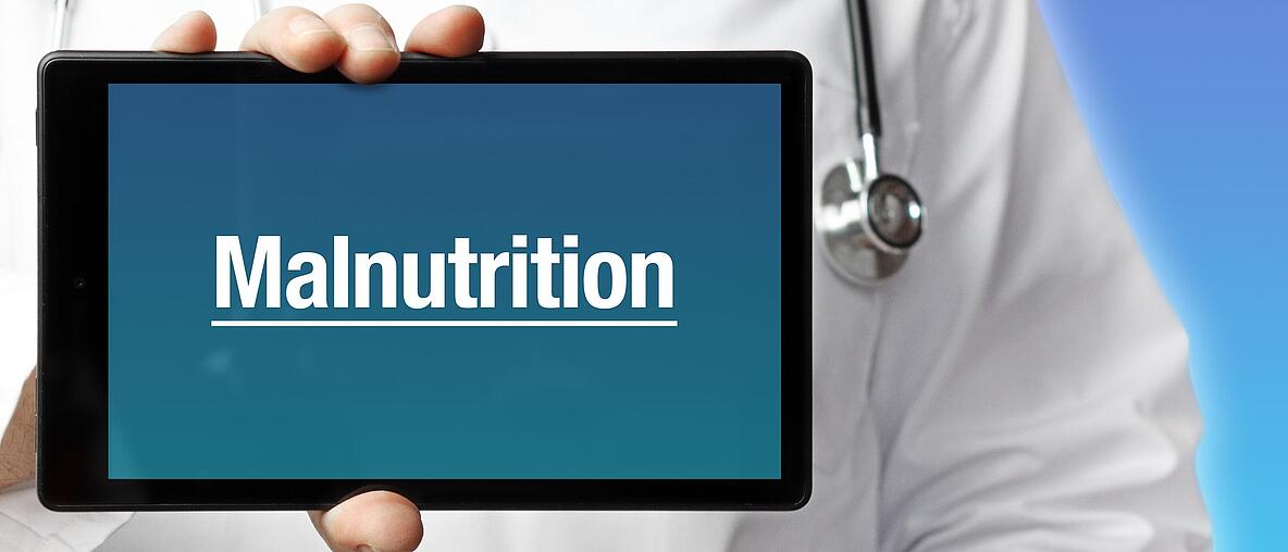 Ein Arzt im Kittel hält einen Tablet-Computer hoch. Auf dem Display steht der Begriff „Malnutrition“