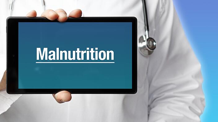 Ein Arzt im Kittel hält einen Tablet-Computer hoch. Auf dem Display steht der Begriff „Malnutrition“