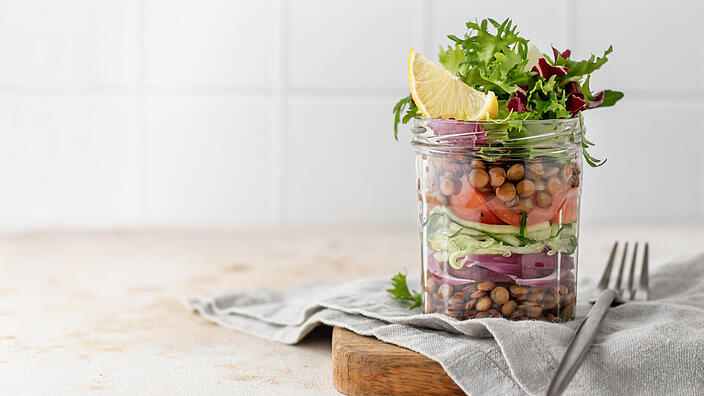 Salat mit Linsen und Gemüse in einem Glas mit Gabel auf Küchentisch.
